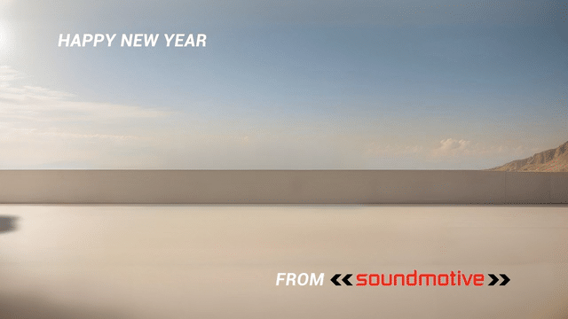 On a coastal highway a sports car drives in front of a wall as it passes it completes the words "Happy New Year - get in top gear with visuals - from Sound Motive"